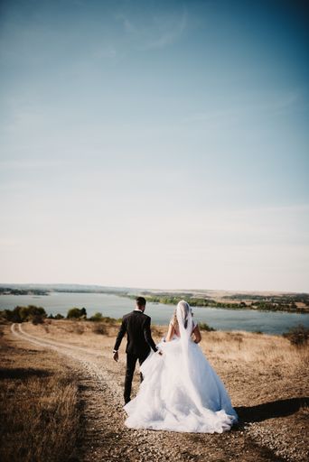 A serene view of a bride in a beautiful wedding dress and the groom walking on the shore of a lake