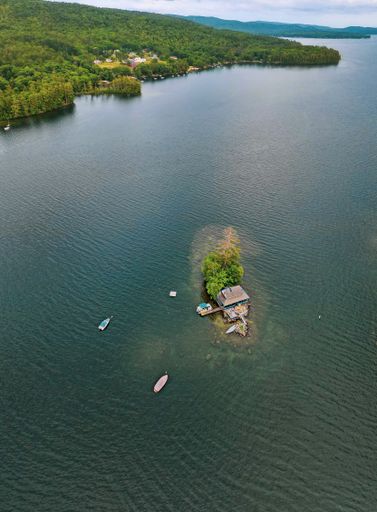 An aerial view of a small island in the middle of the water with a fishing cabin and bats