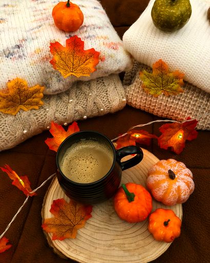 A vertical shot of a cup of hot coffee with tiny pumpkins and dried leaves on the table