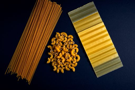 A high angle closeup shot of different types of raw pasta on a dark background