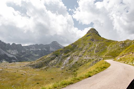 A beautiful country landscape with a road surrounded by green mountains under a cloudy sky