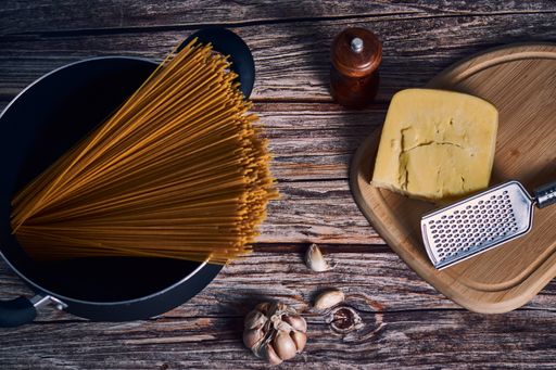 An overhead shot of spaghetti, onions, garlic, cheese, pepper on a wooden table