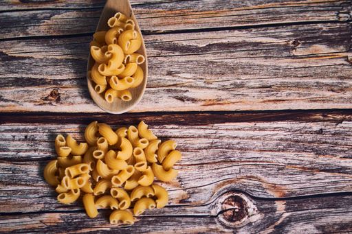 An overhead closeup shot of macaroni and a wooden spoon on a wooden table