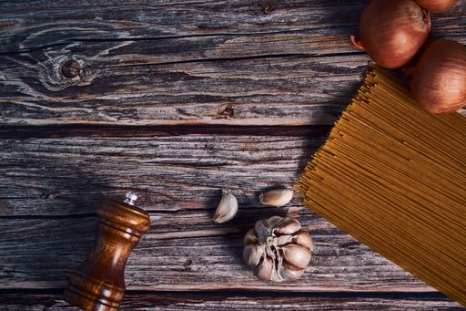 An overhead shot of spaghetti, onions, garlic, and pepper on a wooden table