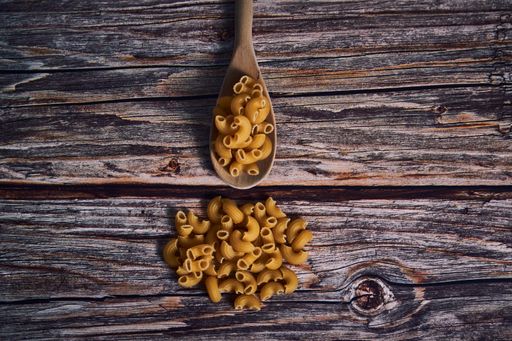 An overhead closeup shot of macaroni and a wooden spoon on a wooden table
