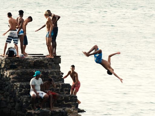 A group of young people jumping into the sea from the Fort of Santa Maria pier in Salvador, Brazil