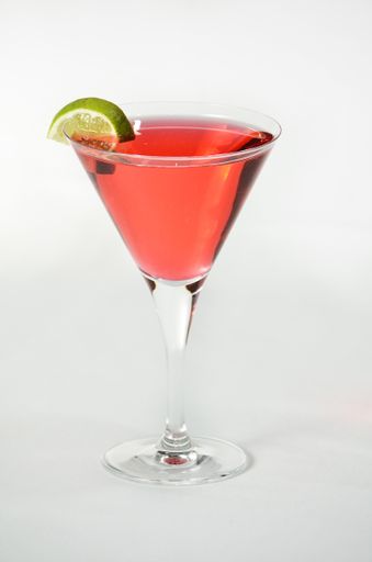 A vertical shot of a pink liquid in a Martini glass with a twist of lime on top on a white background