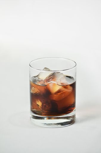 A vertical shot of a glass filled with ice and brown colored liquid with a white background