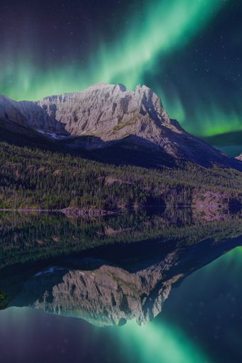 A stunning view of the Northern Lights over a mountain range with a perfect reflection in a calm lake.