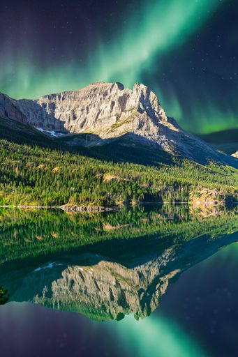 Breathtaking view of the Northern Lights over a mountain reflected in a serene lake, showcasing nature's beauty at night.