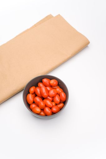 dark gray stoneware bowl full of datterini tomatoes and kraft paper on a white surface with text space