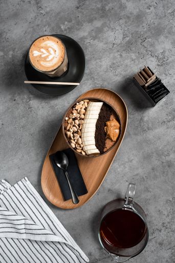 A vertical top view of a delicious meal with banana, nuts, and peanut butter in a bowl