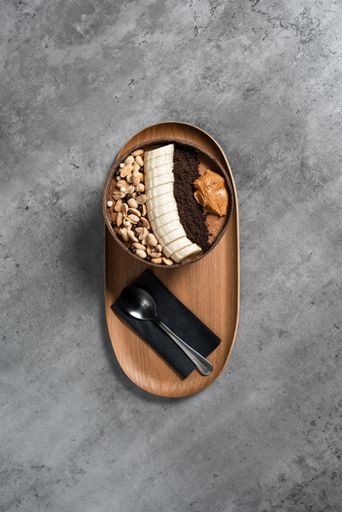 A vertical top view of a delicious meal with banana, nuts, and peanut butter in a bowl