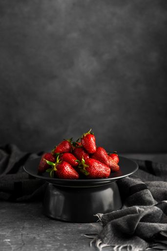 A vertical shot of fresh strawberries on a black plate with a monochrome background