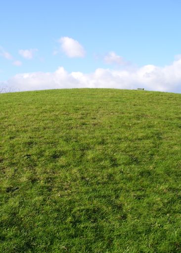 A mesmerizing view of a hill covered with dense green grass against a cloudy sky on a sunny day