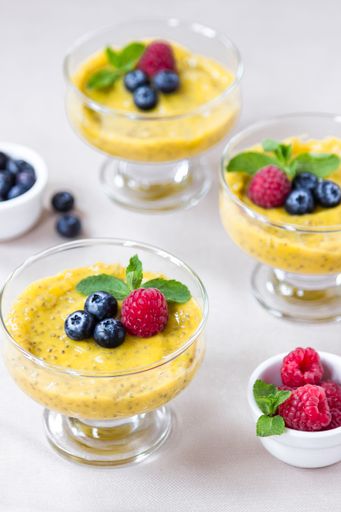 A vertical shot of tasty mango chia pudding with raspberries served in glass jars