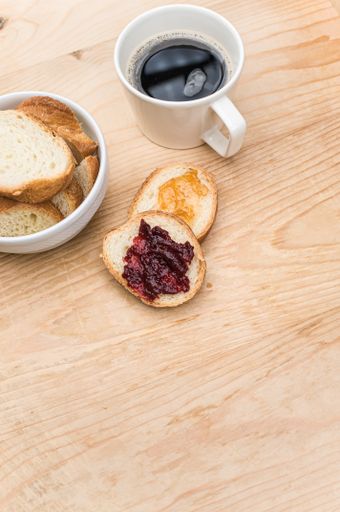 organic fresh sliced bread in a white bowl jam and coffee cup on a wooden tabletop with copy space