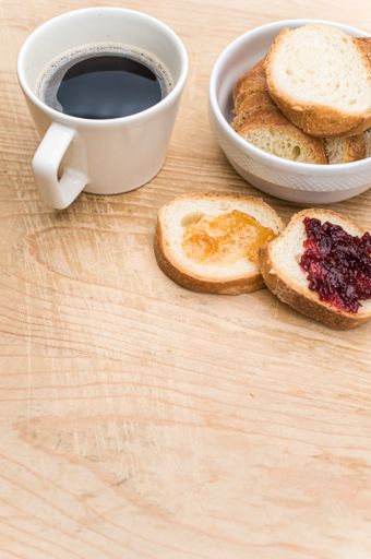 organic fresh sliced bread in a white bowl jam and coffee cup on a wooden tabletop with copy space