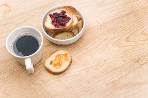 organic fresh sliced bread in a white bowl jam and coffee cup on a wooden tabletop with copy space