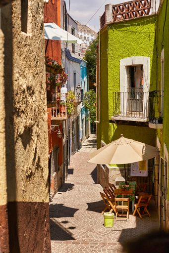 A vertical shot of an empty narrow alley between old buildings with balconies on a sunny day
