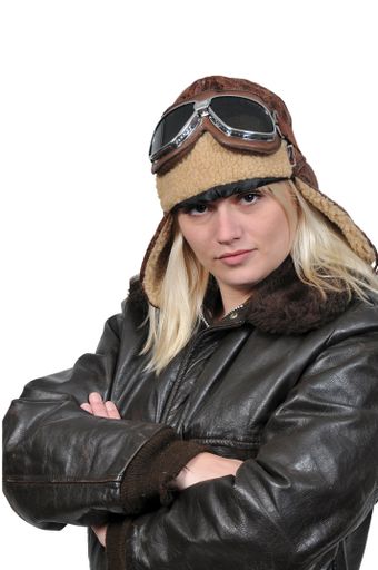 A vertical shot of a pretty white woman wearing a vintage pilot helmet with goggles