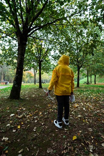 A vertical shot of a little Caucasian boy in a yellow coat holding a drone and remote control in the park