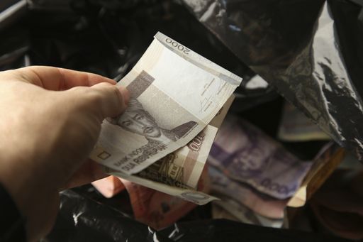 Various currencies being thrown into a black plastic trash bag. International economic crisis concept image.