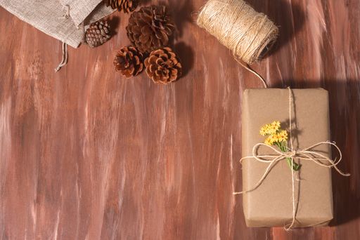 A top view of a wrapped Christmas present on a wooden table with pine cones and a twine string