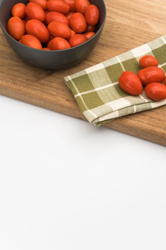 dark gray bowl full of datterini tomatoes with chopping board and table napkin on a white surface with text space