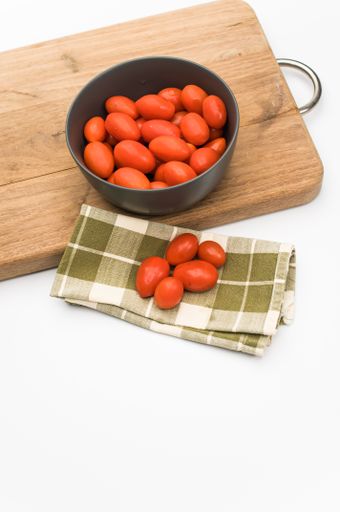 dark gray bowl full of datterini tomatoes with chopping board and table napkin on a white surface with text space