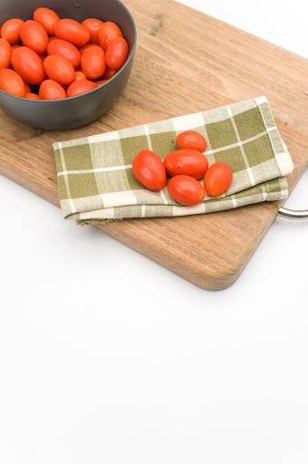 dark gray bowl full of datterini tomatoes with chopping board and table napkin on a white surface with text space