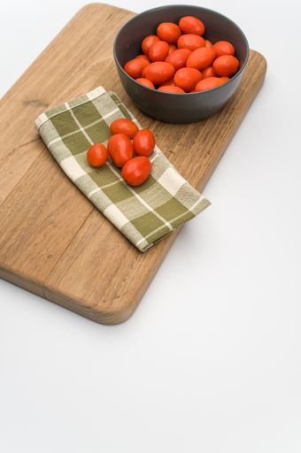 dark gray bowl full of datterini tomatoes with chopping board and table napkin on a white surface with text space