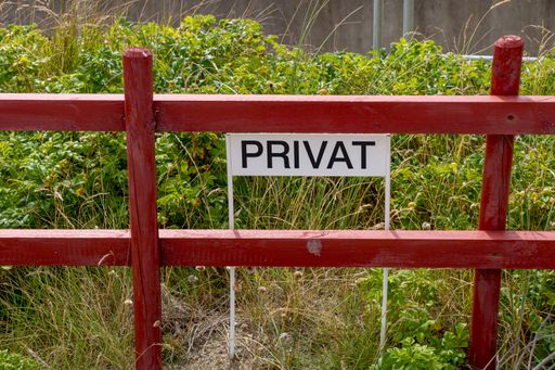 A red fence and green grass with privat sign