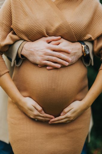A Vertical shot of a pregnant woman with a man holding the belly