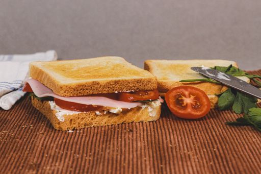 A closeup of sandwiches with toast bread, tomatoes, ham, and parsley.