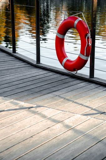 A vertical shot of a red lifebuoy hanging on the rails of a pier