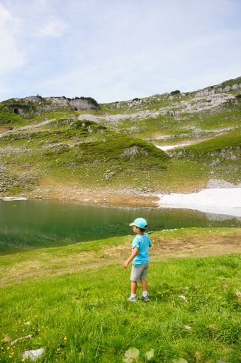 A young boy standing in front of the small lake surrounded by rocky hills