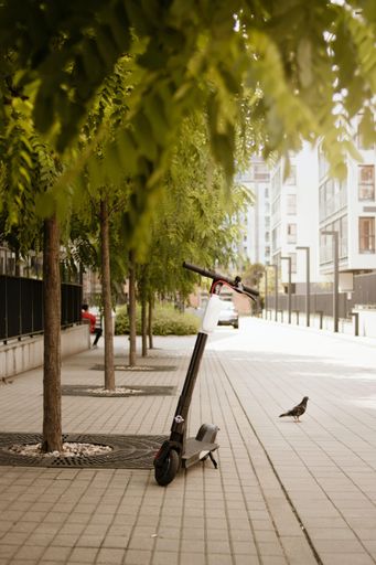 A vertical shot of an electric scooter parked under the tree
