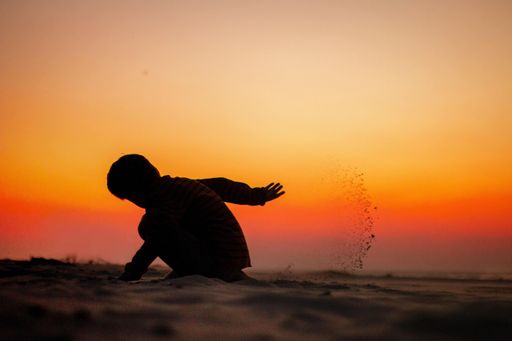 The sillhouette of a child playing with sand during the sunset