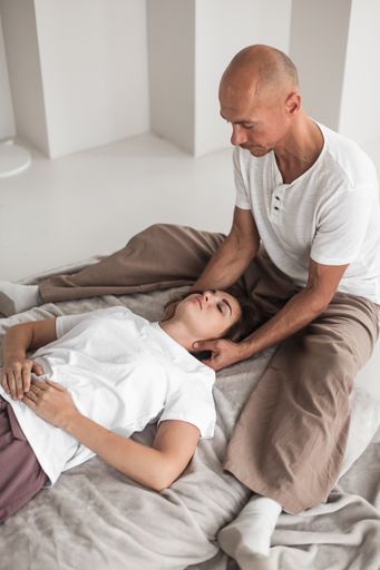 A middle-aged Caucasian bald masseur and a woman doing Japanese neck massage exercises on a mat at home