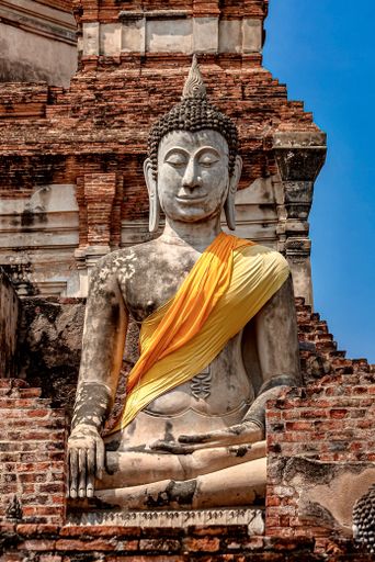 A vertical shot of an old Buddha statue covered with yellow and orange cloth