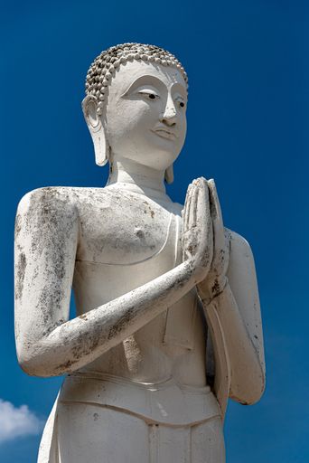 A vertical shot of an old Buddha statue with a clear blue sky in the background