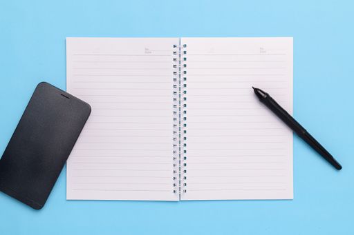 A top view of an Electronic pen, smartphone and a notebook on a blue background
