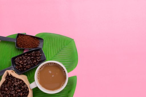 A top view of a Coffee mug and coffee beans on a pink background