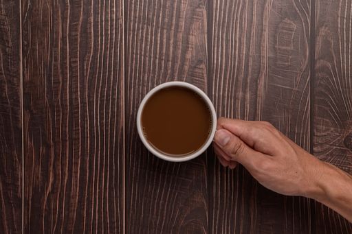 A top view of a Hand holding a coffee mug on a wood background