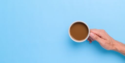 A top view of a Hand holding a coffee mug on a blue background with a copy space