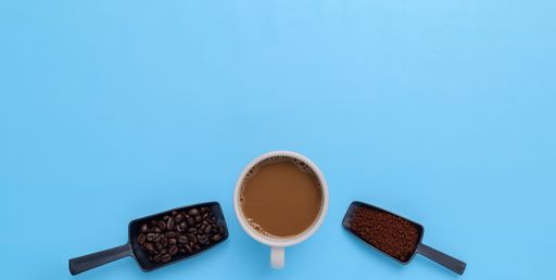 A top view of a Coffee mug, coffee beans, ground coffee on a blue background with a copy space