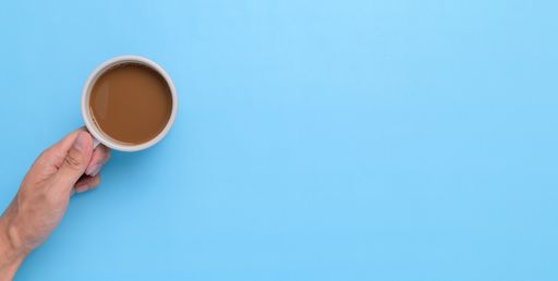 A top view of a Hand holding a coffee mug on a blue background with a copy space