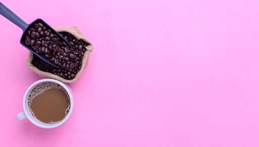 A top view of a Coffee mug and coffee beans on a pink background with a copy space