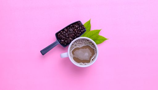 A top view of a Coffee mug and coffee beans on a pink background with a copy space